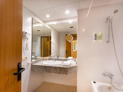 Helles Badezimmer mit großer Spiegelwand, Doppelwaschbecken und Badewanne mit Duschkopf