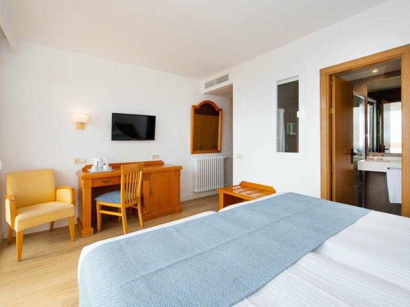 Helles Hotelzimmer mit Doppelbett, Schreibtisch, Stuhl und Fernseher an der Wand.