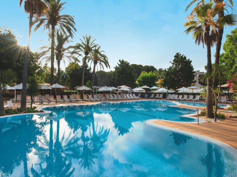 Ein einladender Poolbereich mit Palmen und Liegestühlen unter blauem Himmel.