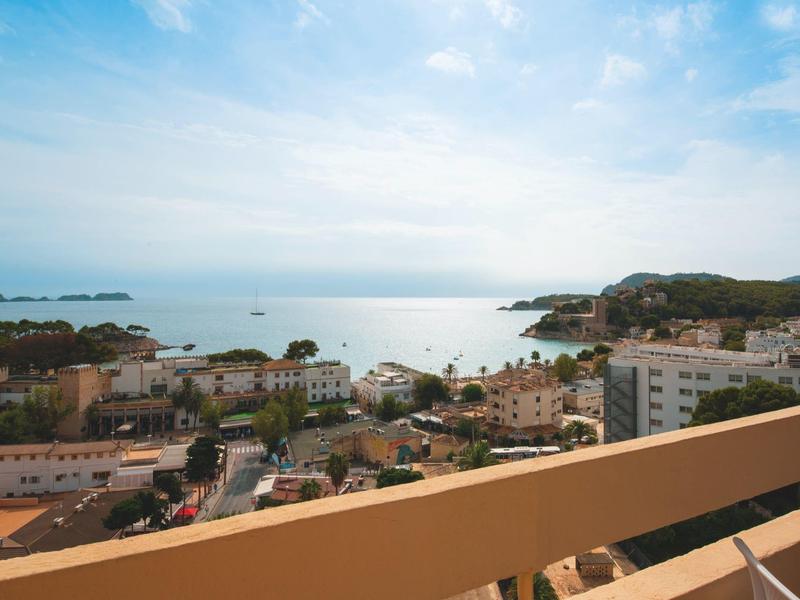 Blick von einem Hotelbalkon auf eine Küstenstadt mit Meer und bewölktem Himmel.
