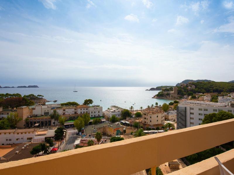 Blick von einem Balkon auf ein Küstenstädtchen mit Meer und bewölktem Himmel.