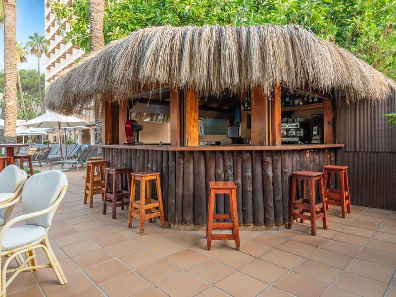 Eine tropische Bar mit Strohdach und Holztheke im Außenbereich eines Hotels.