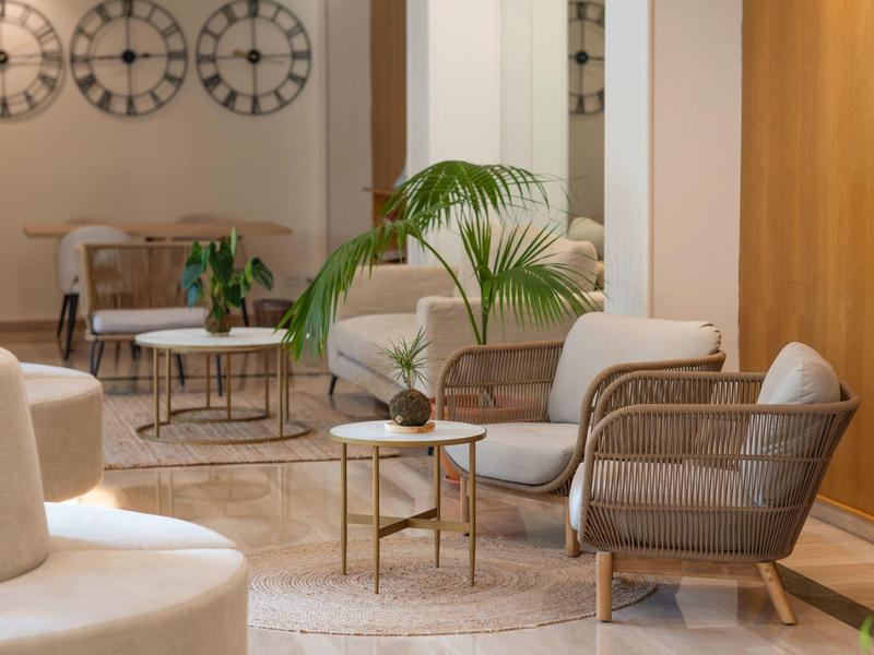 Gemütlicher Wartebereich mit Stühlen, Tischen und übergroßer Pflanze in einem Hotel.