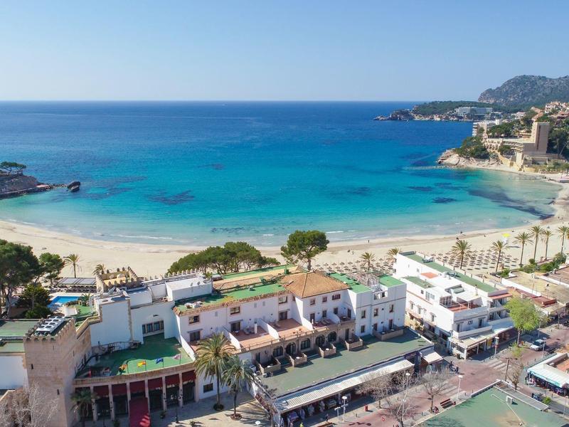 Blick auf einen belebten Küstenort mit Sandstrand, blauem Meer und umliegenden Gebäuden.