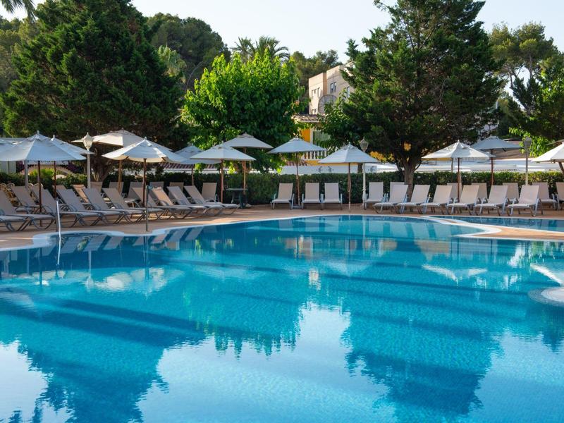 Großer Außenpool mit Liegestühlen und Sonnenschirmen, umgeben von Bäumen.