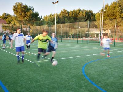 Bambini che giocano a calcio su un campo in erba sintetica all'aperto al tramonto.