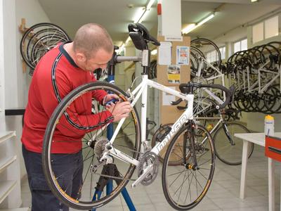 Uomo che ripara una bici da corsa in officina con molte bici da corsa.