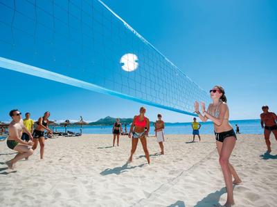 Personas juegan voleibol de playa bajo el sol en arena con cielo azul despejado.