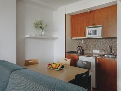 Pequeña cocina moderna con armarios de madera, mesa de comedor y cesta de frutas en un apartamento de hotel.