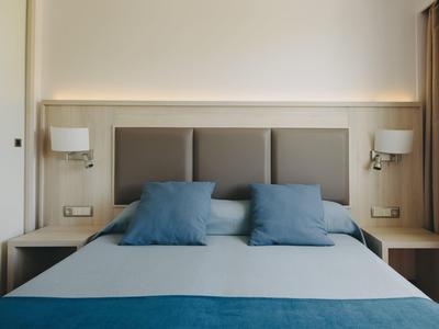 Habitación de hotel moderna con cama doble, cabecera gris y cojines y manta azules.