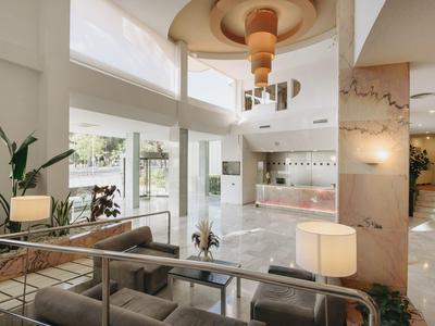 Lobby de hotel luminosa con sofás, lámparas y grandes ventanales con vista a la terraza exterior.