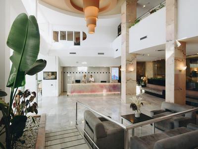 Recepción de hotel moderna y luminosa con suelo de mármol blanco y áreas de estar elegantes.