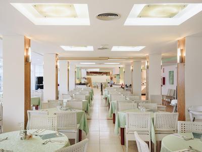 Restaurante amplio y luminoso con mesas y sillas blancas, ideal para huéspedes del hotel.