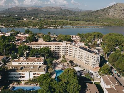 Complesso alberghiero con piscina vicino a un lago, circondato da alberi e montagne sullo sfondo.