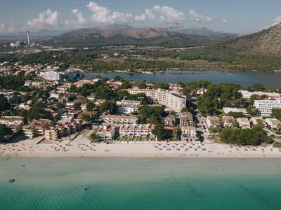 Vista aérea de un hotel con playa, agua turquesa clara y montañas al fondo.