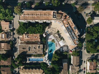 Vista aérea de un hotel con piscina y árboles circundantes en un barrio urbano.