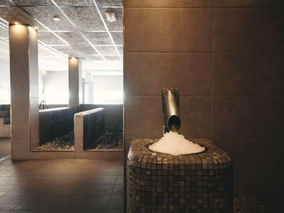 Baño de vapor minimalista con paredes claras, baldosas marrón oscuro y salida de vapor sobre pedestal de mosaico.