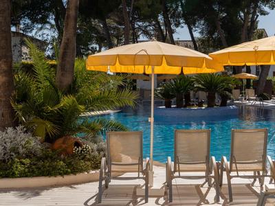 Cuatro tumbonas con sombrillas amarillas junto a una piscina azul de hotel en un jardín tropical.