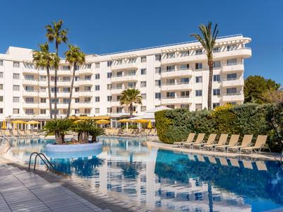 Complejo hotelero moderno con piscina, tumbonas y palmeras bajo un cielo azul claro.