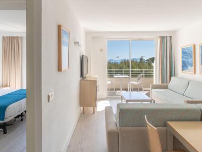 Sala luminosa con sofá, mesa y acceso a balcón con vista a paisaje verde.