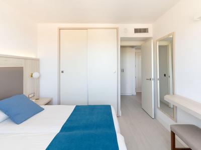 Habitación de hotel luminosa con cama doble, manta azul, armario y puerta abierta.
