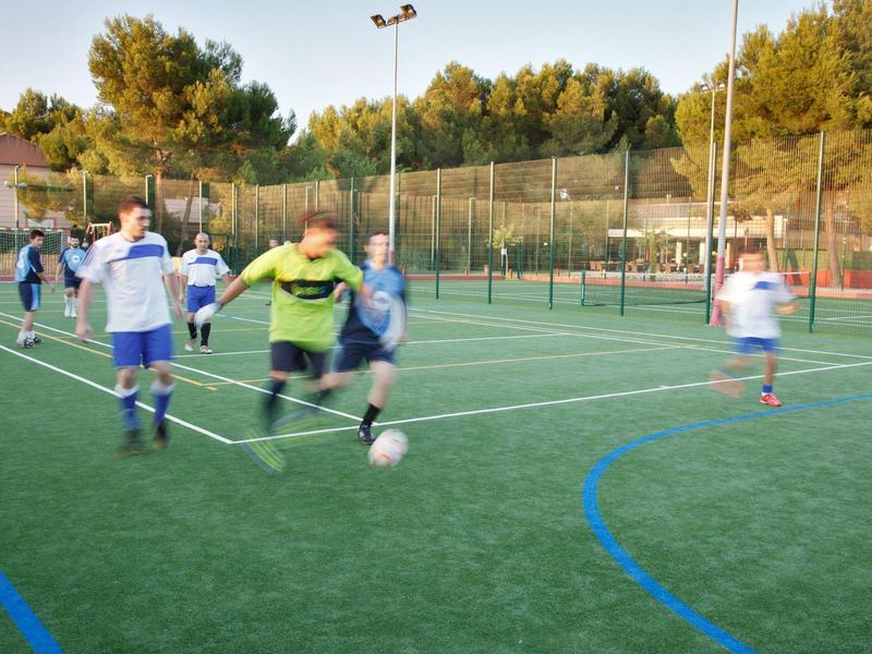Niños juegan al fútbol en un campo de césped artificial de un resort vacacional al atardecer.