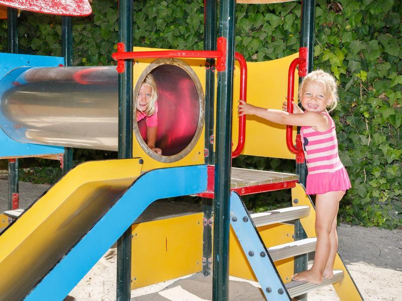 Niños jugando en un colorido parque infantil al aire libre con tobogán y túnel.