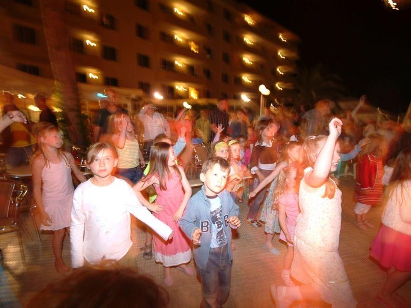 Niños bailan al aire libre por la noche frente a un hotel iluminado.