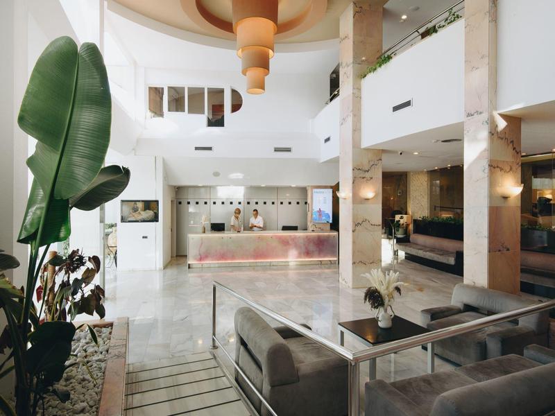 Recepción de hotel moderna y luminosa con suelo de mármol blanco y áreas de estar elegantes.