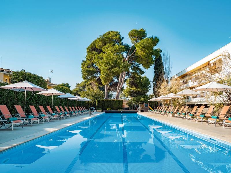 Una piscina larga y azul con tumbonas y sombrillas a ambos lados bajo un cielo despejado.