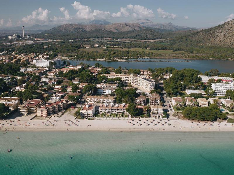 Vista aérea de un hotel con playa, agua turquesa clara y montañas al fondo.