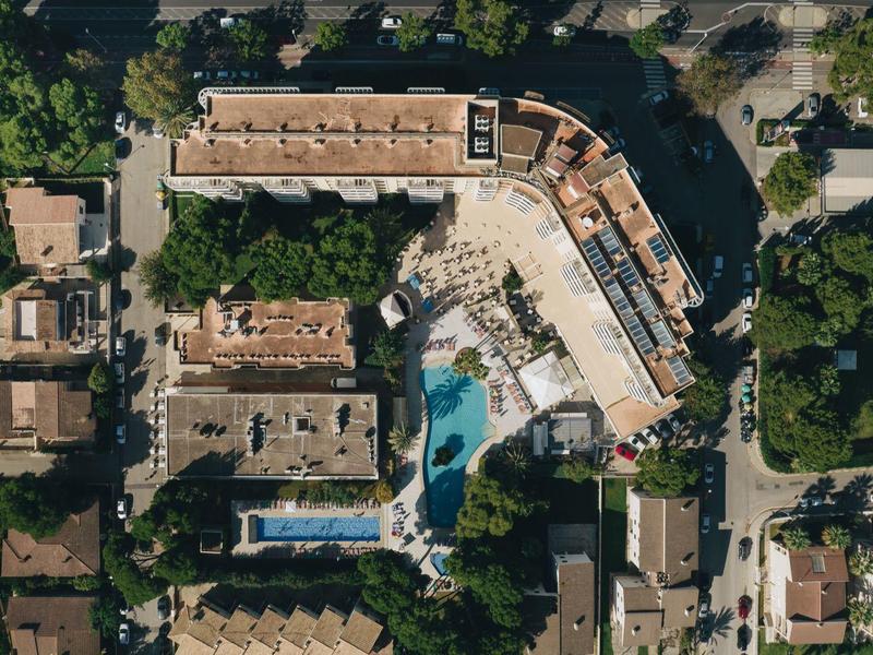Vista aérea de un hotel con piscina y árboles circundantes en un barrio urbano.