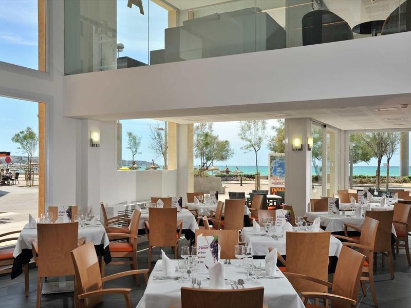 Nowoczesna restauracja z dużymi oknami z widokiem na basen i palmy.