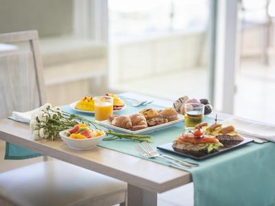 Tisch mit gedecktem Frühstück, Croissants, Marmelade und Obst vor einem Fenster.