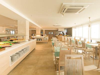 Licht hotelrestaurant met houten stoelen, tafels en buffetgedeelte aan de linkerkant.