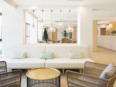 Moderne hotel lobby met witte bank, houten stoelen en ronde tafels onder warme verlichting.