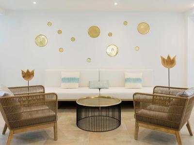 Sala d'attesa elegante con poltrone in rattan, divano bianco e decorazioni dorate a parete.