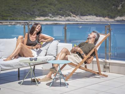 Zwei Frauen entspannen sich auf einer Hotelterrasse mit Meerblick bei sonnigem Wetter.