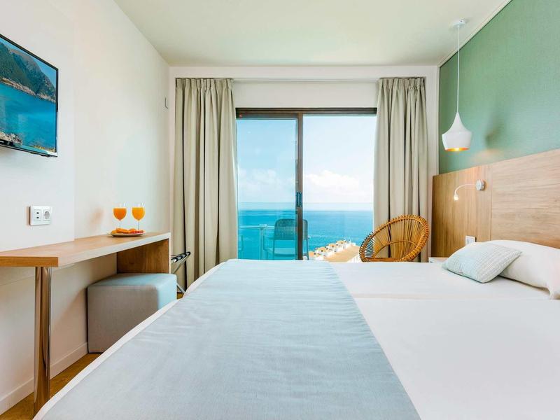 Camera d'hotel con letto grande, vista mare, pareti verdi e arredamento minimalista.