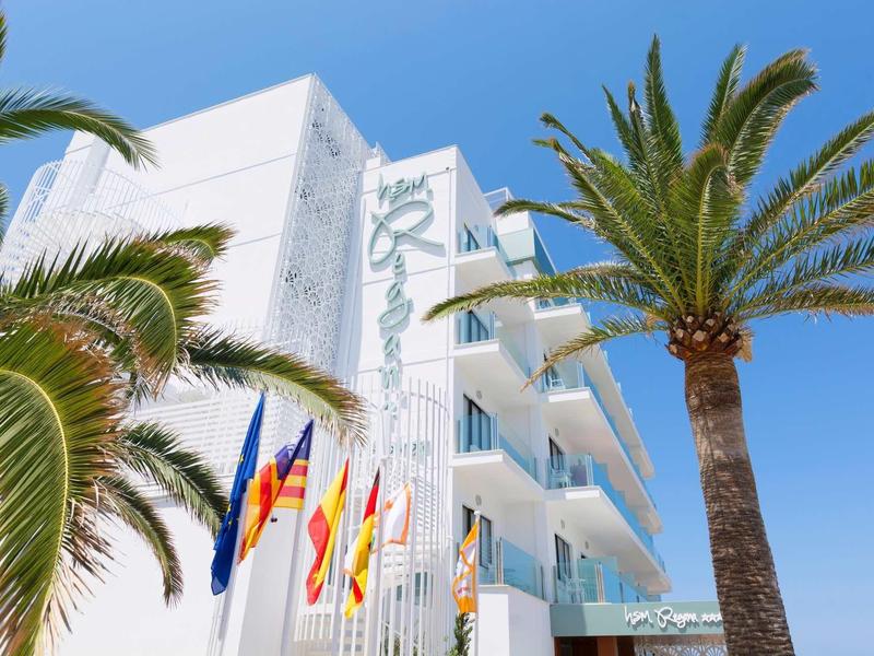 Hotel bianco moderno circondato da palme sotto un cielo azzurro.