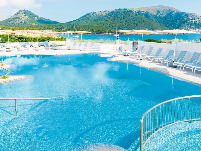 Piscina d'hotel con lettini e montagne sullo sfondo sotto un cielo limpido.