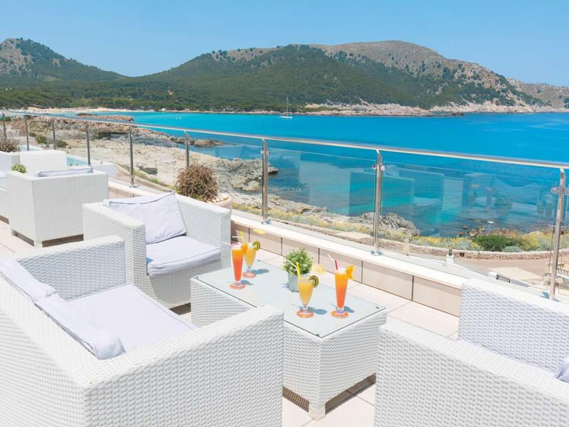 Terrazza dell'hotel con poltrone bianche vista mare turchese e colline.