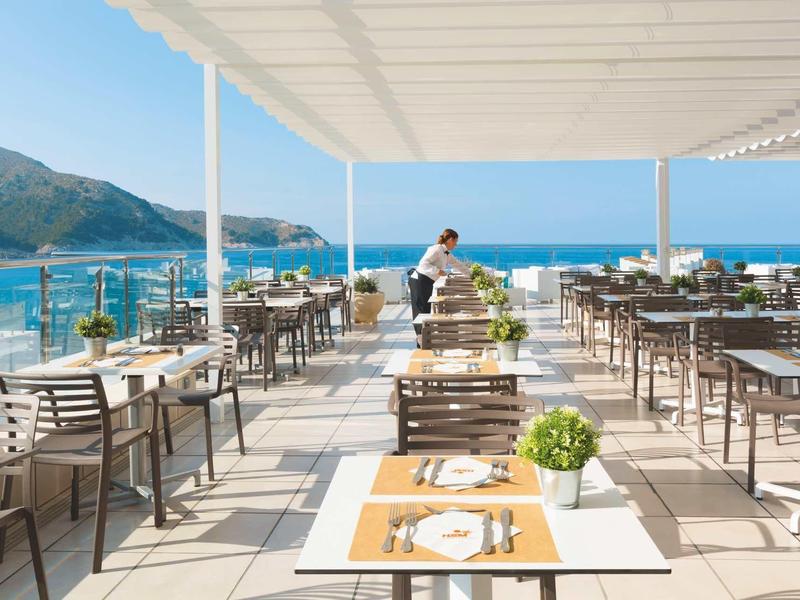 Terrazza del ristorante dell'hotel con vista sul mare e montagne sotto un cielo limpido.