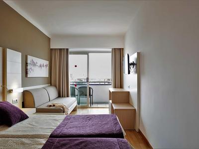 Jasny pokój hotelowy z dwoma łóżkami, fioletowymi kocami i balkonem z krzesłami