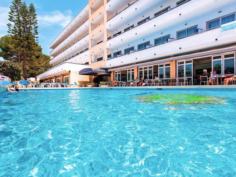 Hotel z dużym odkrytym basenem i wieloma balkonami w słoneczny dzień.