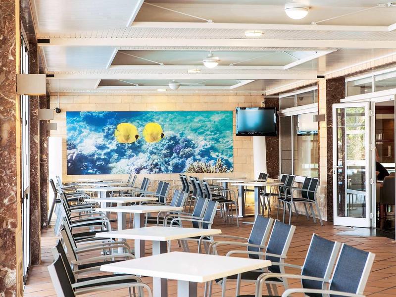 Jasny, nowoczesny salon hotelowy z stołami, krzesłami i kolorową podwodną malowidłem.