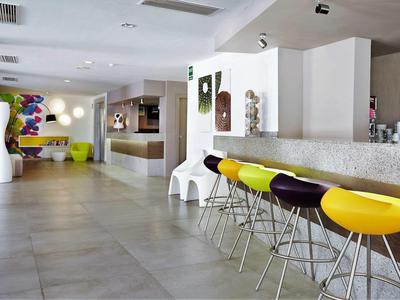 Nowoczesny bar hotelowy z kolorowymi stołkami i jasnymi, minimalistycznymi meblami w otwartej przestrzeni.