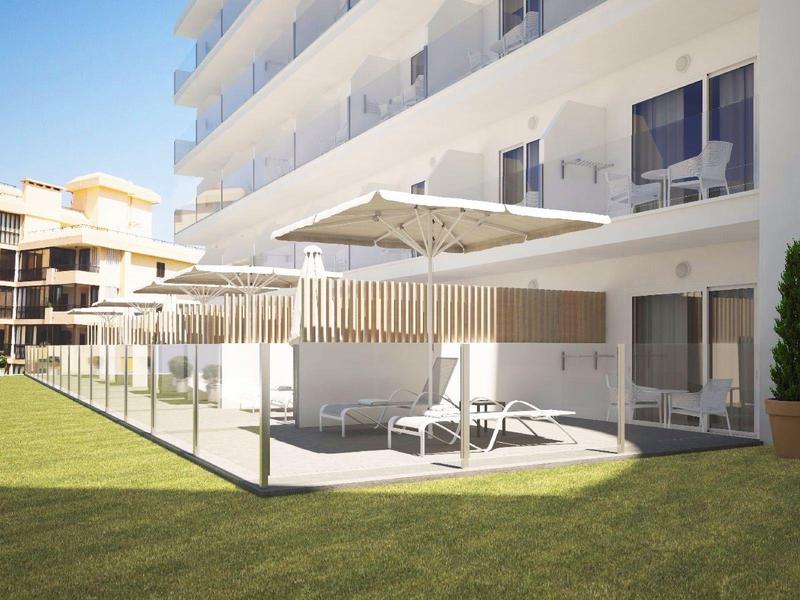 Hotel patio with lounge chairs under a large umbrella and glass railing, surrounded by grass and buildings.