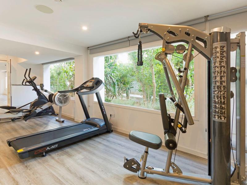 Bright gym with treadmill, elliptical, and multi-gym machine by large windows overlooking greenery.