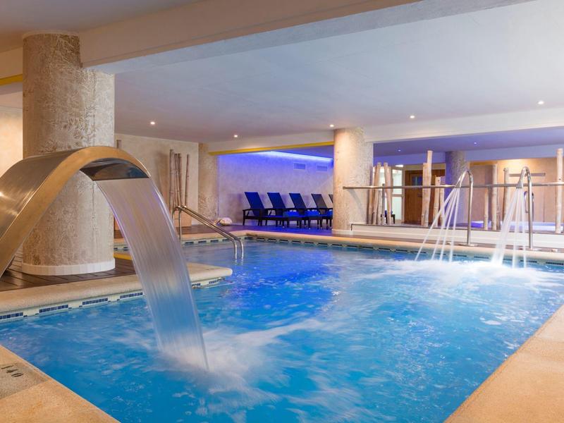 Indoor pool with water features and lounge chairs in a modern hotel spa area.